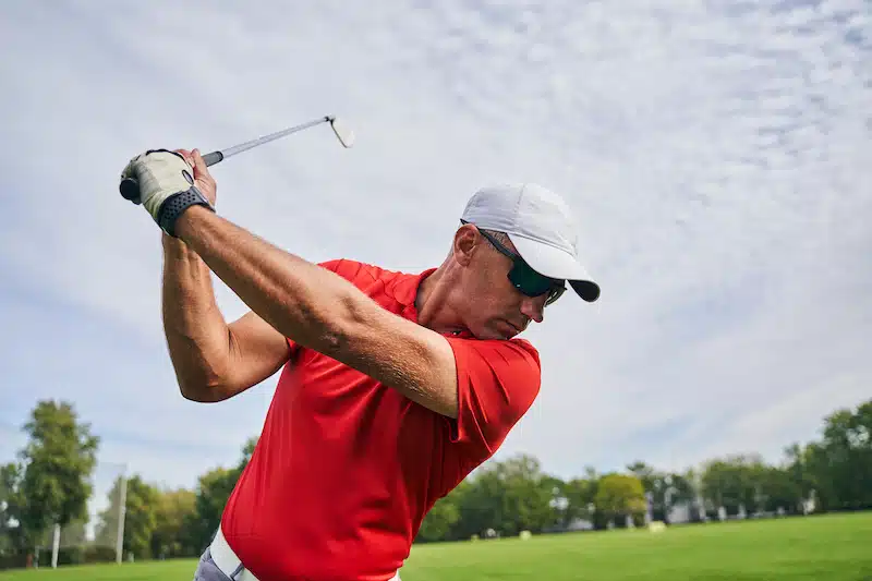 Backswing Front view of a concentrated professional Caucasian sportsman in a cap and sunglasses looking down