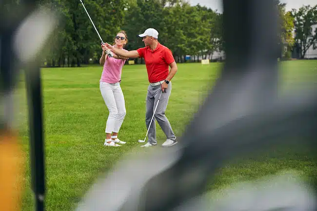 Smiling female beginner taking a golf lesson from a professional